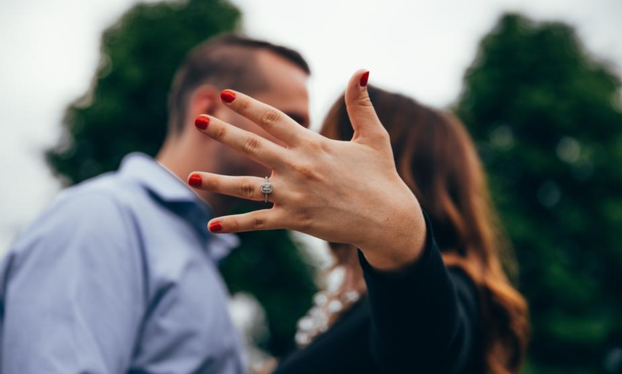 Newly engaged woman showing off her diamond ring close-up while standing with her partner outdoors